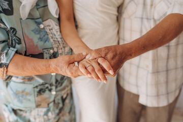 Grandparents hold their granddaughter's hand on their wedding day. A girl's wedding with the support of her parents. Golden wedding ring - obrazy, fototapety, plakaty