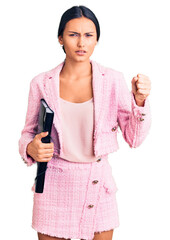 Young beautiful latin girl wearing business clothes holding binder annoyed and frustrated shouting with anger, yelling crazy with anger and hand raised