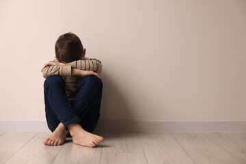 Child abuse. Upset boy sitting on floor near beige wall indoors, space for text - obrazy, fototapety, plakaty