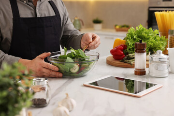 Naklejka premium Man cooking salad at white marble countertop in kitchen, closeup