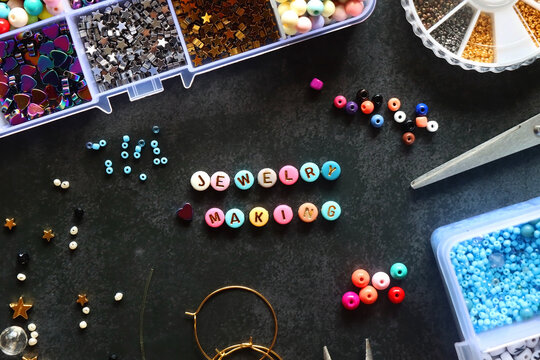 Colorful beads and various jewelry making supplies on dark background. Letter beads spelling JEWELRY MAKING. Top view.