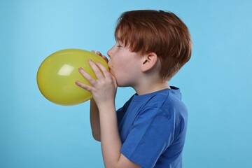 Fototapeta na wymiar Boy inflating yellow balloon on light blue background