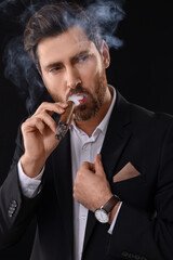 Handsome man in elegant suit smoking cigar on black background