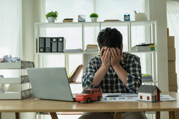 A young Asian man is stressed about bills, car payments, house payments, and holds his head in his...