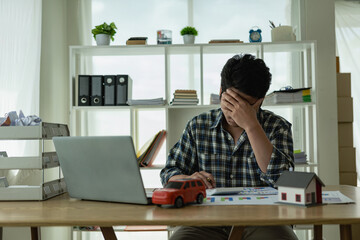 A young Asian man is stressed about bills, car payments, house payments, and holds his head in his...