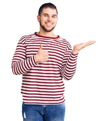 Young handsome man wearing striped sweater showing palm hand and doing ok gesture with thumbs up, smiling happy and cheerful