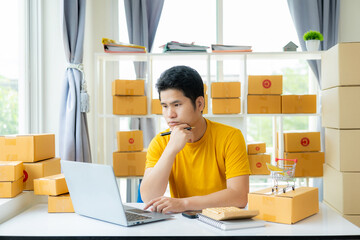 A young Asian male SME business owner sells products online and prepares product packaging boxes for sending online orders and having customers at home who are shopping online ready for delivery.