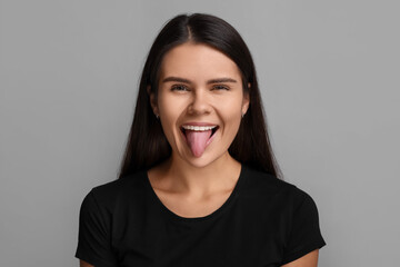 Personality concept. Emotional woman showing tongue on grey background