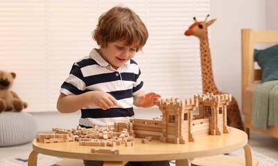 Fototapeta na wymiar Little boy playing with wooden entry gate at table in room. Child's toy