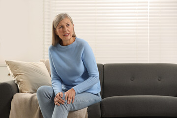 Mature woman suffering from knee pain on sofa at home. Rheumatism symptom