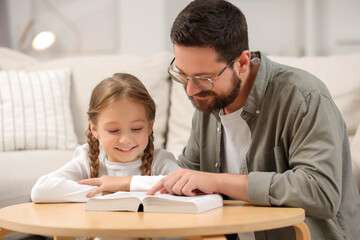 Girl and her godparent reading Bible together at table in room