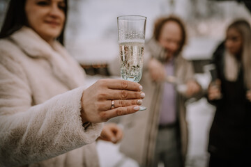 close-up of a woman's hand holding a champagne glass with people in the background, indicating a...
