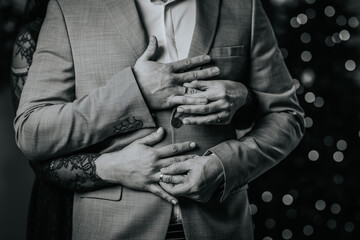 monochrome close-up of a couple's hands clasped around a man in a suit, with the woman's hand...