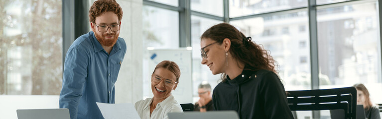 Group of young business people discussing something and smiling while sitting at the office table