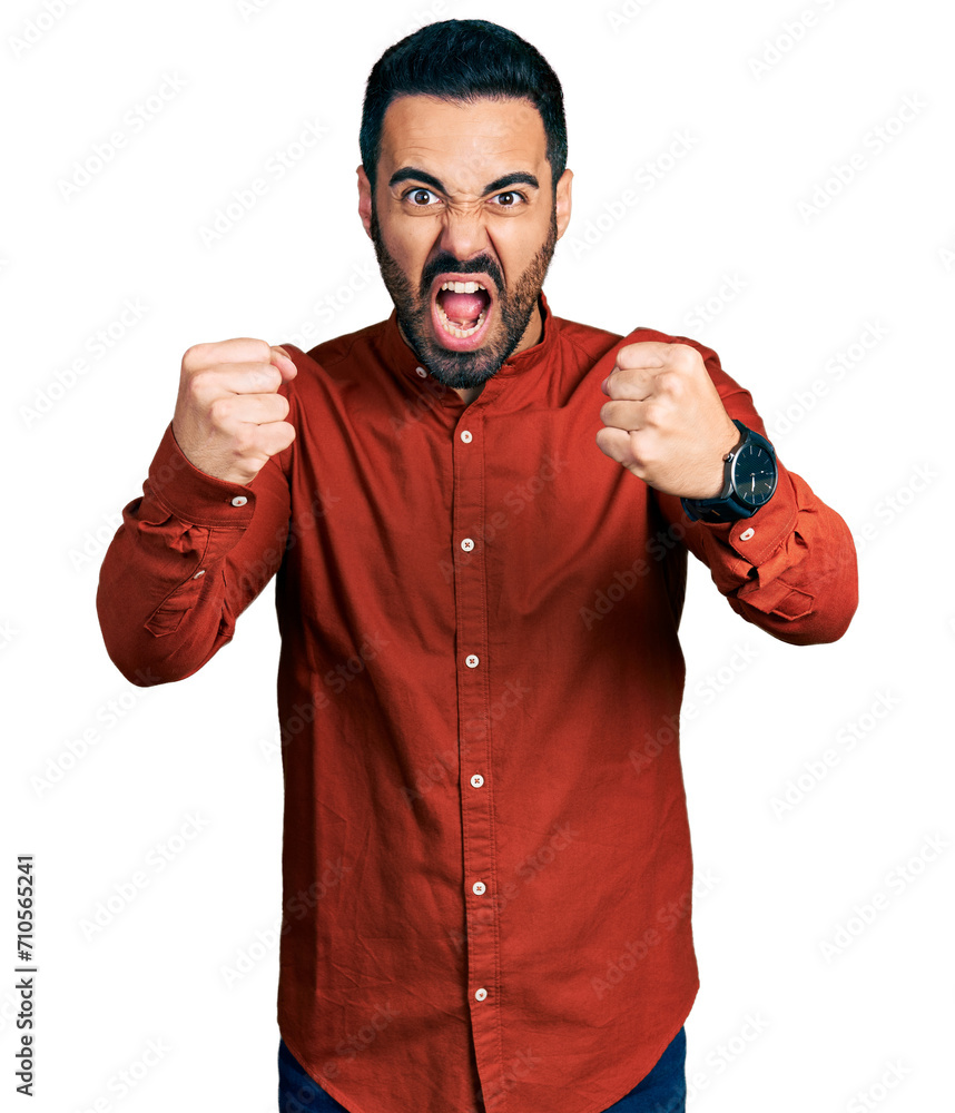 Poster Young hispanic man with beard wearing casual shirt angry and mad raising fists frustrated and furious while shouting with anger. rage and aggressive concept.