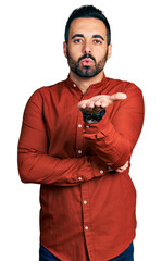 Young hispanic man with beard wearing casual shirt looking at the camera blowing a kiss with hand on air being lovely and sexy. love expression.