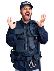 Young hispanic man wearing police uniform celebrating mad and crazy for success with arms raised...