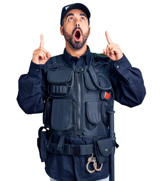 Young hispanic man wearing police uniform amazed and surprised looking up and pointing with fingers and raised arms.
