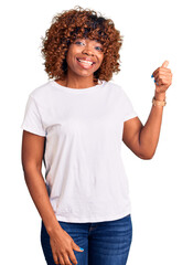 Young african american woman wearing casual white tshirt smiling with happy face looking and pointing to the side with thumb up.