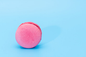 Pink french macaroon or macaron on blue background. Tasty colorful macarons. Cookie made of two smooth halves, fastened with stringy fillings. French pastry made from egg whites.