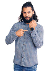 Young arab man wearing casual clothes in hurry pointing to watch time, impatience, looking at the...