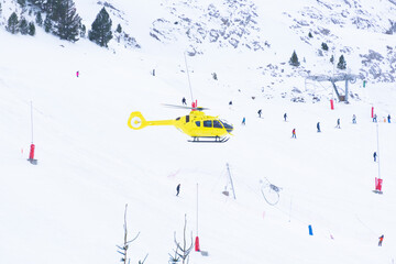 yellow rescue helicopter flies over ski slopes, with skiers. photography in the pyrenees spain