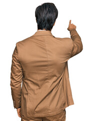 Young hispanic man wearing business clothes posing backwards pointing ahead with finger hand