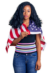Beautiful african american woman holding united states flag thinking attitude and sober expression looking self confident