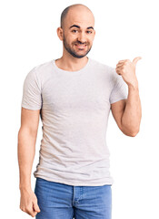 Young handsome man wearing casual t shirt smiling with happy face looking and pointing to the side with thumb up.