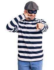 Young handsome man wearing burglar mask smiling doing talking on the telephone gesture and pointing to you. call me.