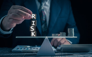 Economic risk management concept. Businessman holding wooden block with word "RISK". With level coin balance, banking, financial crisis, bad debt, inflation and interest rates. Investment protection.