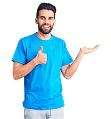 Young handsome man with beard wearing casual t-shirt showing palm hand and doing ok gesture with thumbs up, smiling happy and cheerful