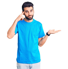 Young handsome man with beard wearing casual t-shirt confused and annoyed with open palm showing copy space and pointing finger to forehead. think about it.