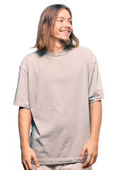 Handsome caucasian man with long hair wearing casual clothes looking away to side with smile on face, natural expression. laughing confident.