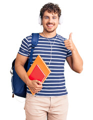 Young handsome man with curly hair holding student backpack and books smiling happy and positive,...