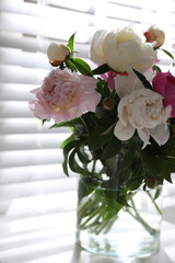 Beautiful peonies in vase on table near window indoors