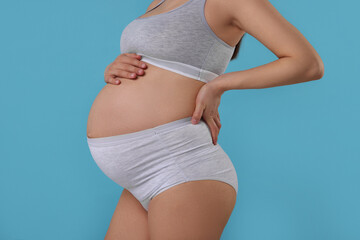 Pregnant woman in comfortable maternity underwear on light blue background, closeup