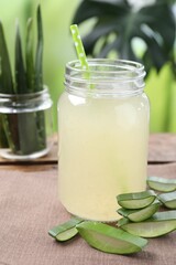 Fresh aloe juice in jar with straw and cut leaves on wooden table outdoors, closeup