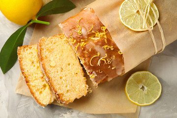 Cut tasty lemon cake with glaze and citrus fruits on light grey textured table, flat lay