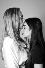 tender black and white portrait of a mother with closed eyes kissing her teenage daughter on the forehead