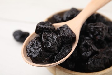 Bowl and spoon with sweet dried prunes on white table, closeup