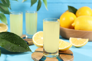 Tasty limoncello liqueur, lemons and green leaves on light blue table
