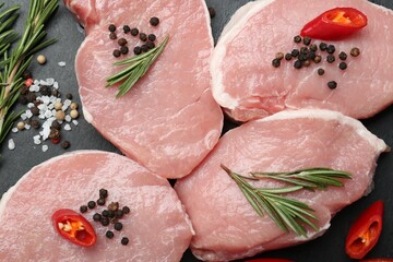 Pieces of raw pork meat, chili pepper and spices on board, closeup