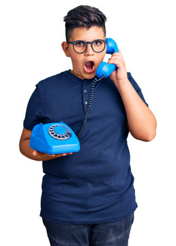 Little boy kid using vintage telephone scared and amazed with open mouth for surprise, disbelief face