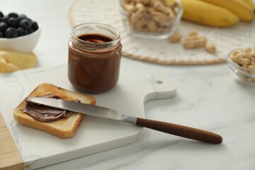 Toast with tasty nut butter, knife and jar on white marble table