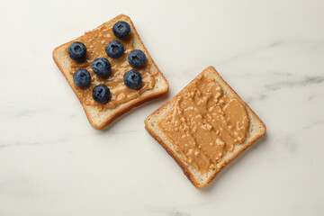Delicious toasts with peanut butter and blueberries on white marble table, flat lay