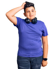 Little boy kid listening to music wearing headphones confuse and wonder about question. uncertain with doubt, thinking with hand on head. pensive concept.