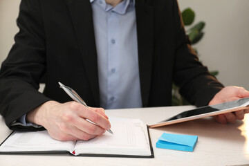 Man taking notes at white wooden table indoors, closeup
