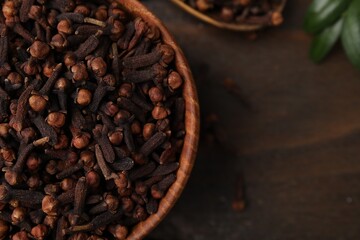 Aromatic cloves in bowl on wooden table, top view. Space for text