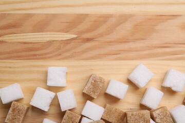 White and brown sugar cubes on wooden table, flat lay. Space for text